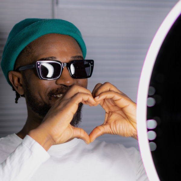 Photo of an influencer making a heart symbol with his hands standing behind a ring light