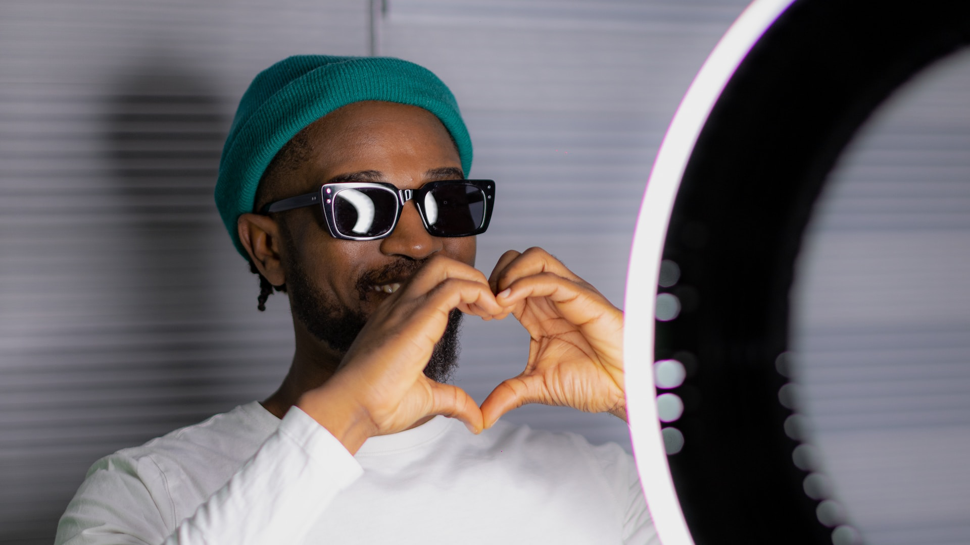 Photo of an influencer making a heart symbol with his hands standing behind a ring light