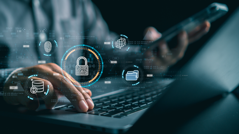 Photo of a person working on a laptop and holding a smartphone with cybersecurity-related icons in the foreground