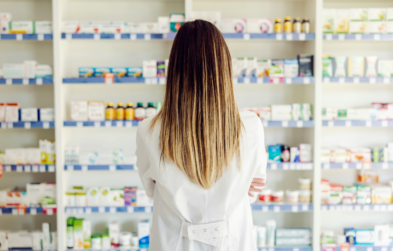 Long haired person stands in front of a wall of over the counter medication