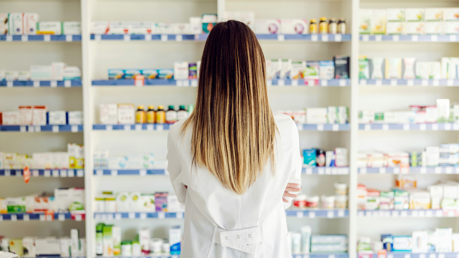 Long haired person stands in front of a wall of over the counter medication