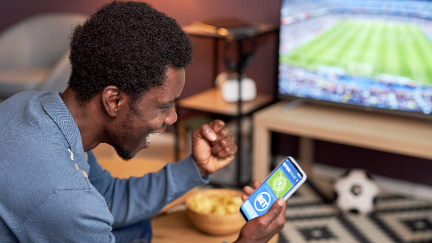 Man cheering at phone showing bet on sport match